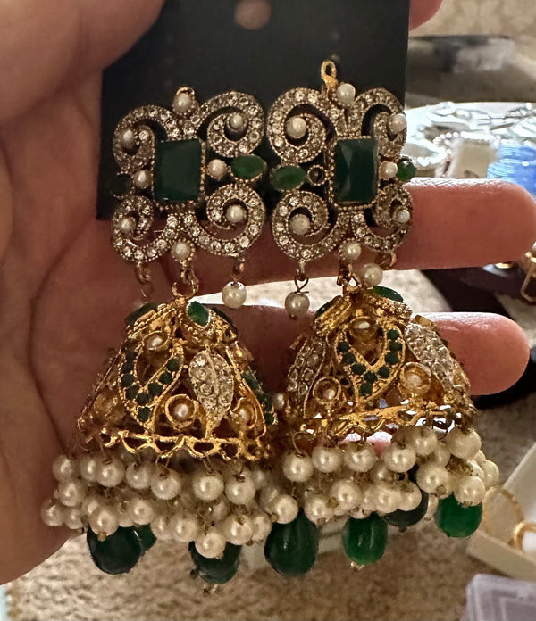 Close-up of green and gold jhumka earrings with pearl-look fringe and green bead drops held in hand