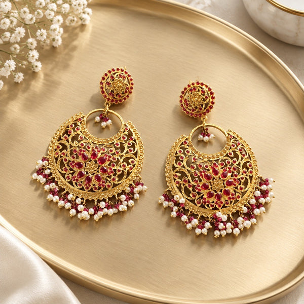 Red gold-tone chandbali earrings with floral stone details and white pearl-style bead drops on a gold tray