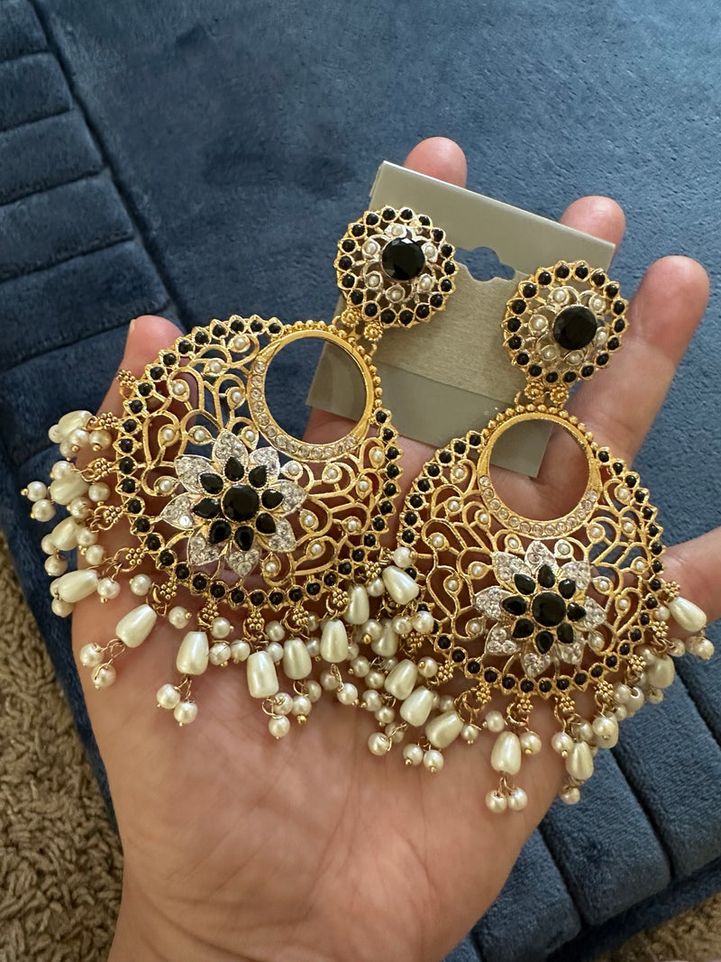 Pair of black and gold-tone floral chandbali earrings with openwork design and ivory pearl-look fringe held in hand