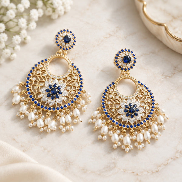 Pair of royal blue floral chandbali earrings with gold-tone openwork and ivory pearl-look fringe on a cream surface