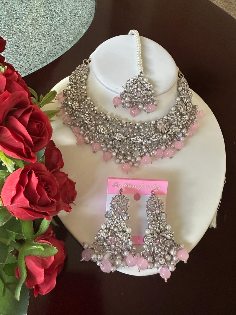 Complete blush pink American diamond floral choker necklace set with matching earrings and tikka displayed with red roses