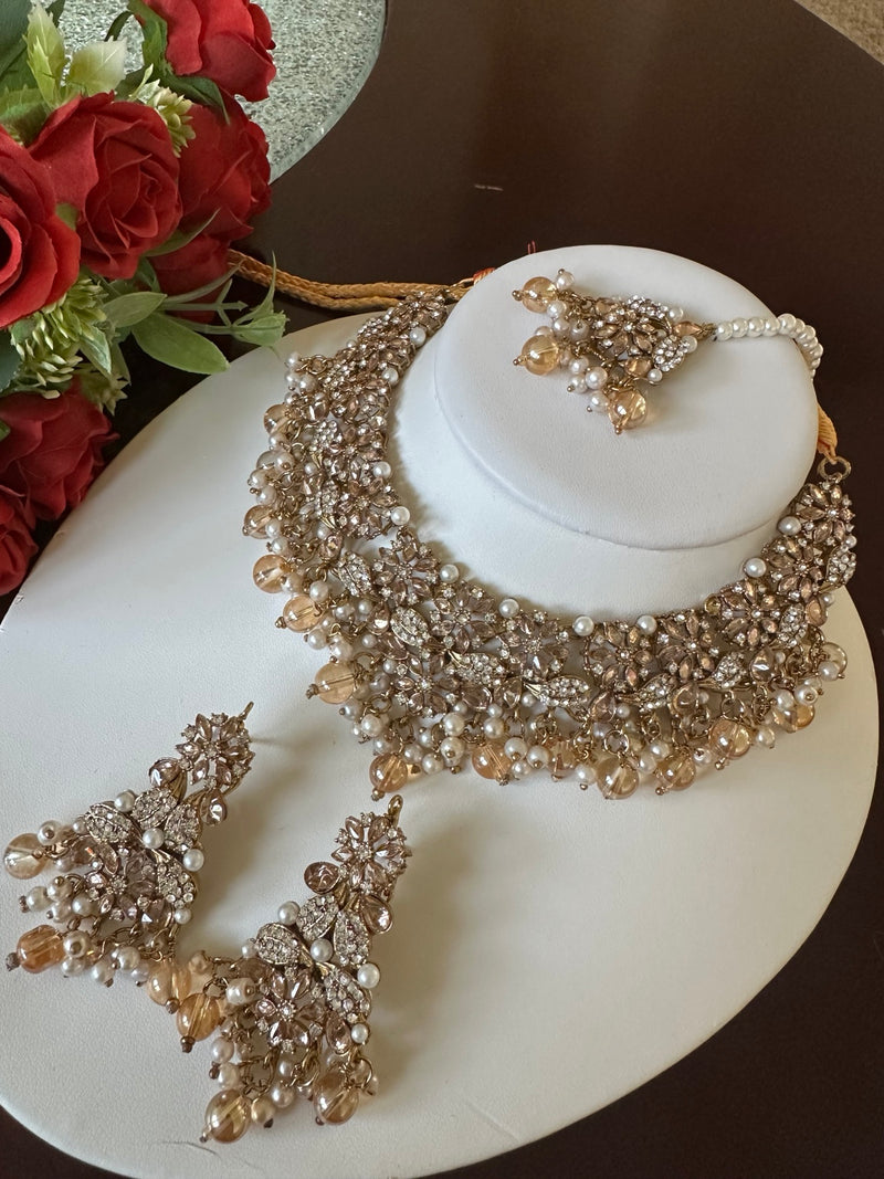 Angled view of champagne gold American diamond floral choker set with matching earrings and tikka