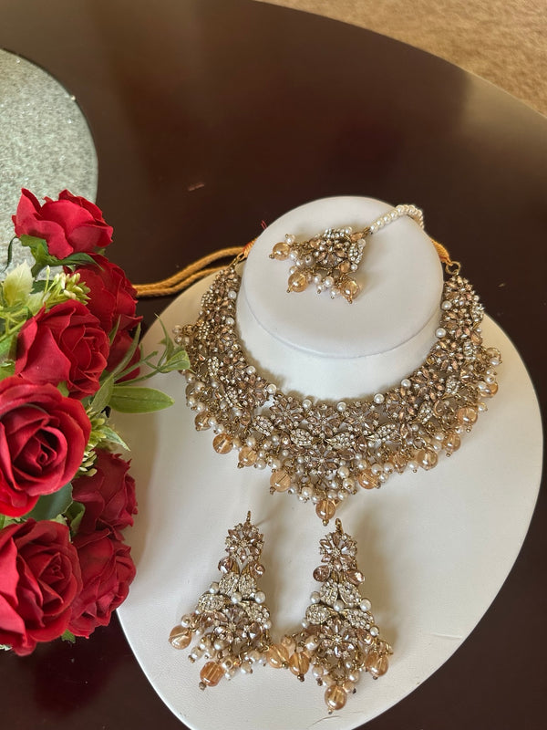 Champagne gold American diamond floral choker necklace set with matching earrings and tikka displayed on a white jewelry bust