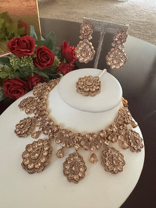 Angled view of champagne rose gold statement necklace set with matching earrings and tikka