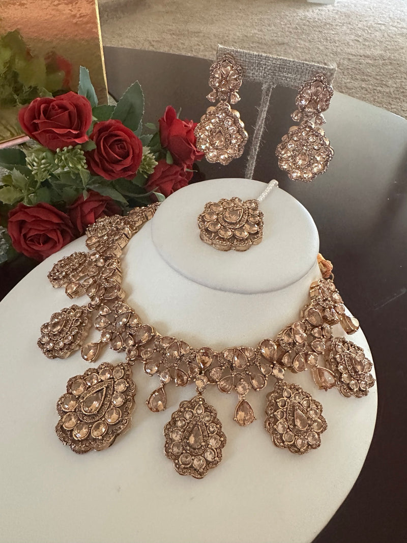 Angled view of champagne rose gold statement necklace set with matching earrings and tikka