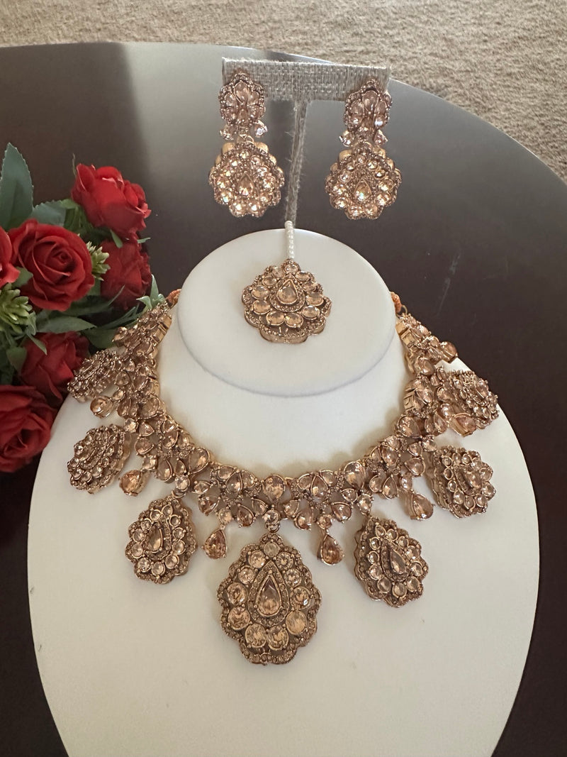 Champagne rose gold necklace with matching crystal earrings and tikka on jewelry display