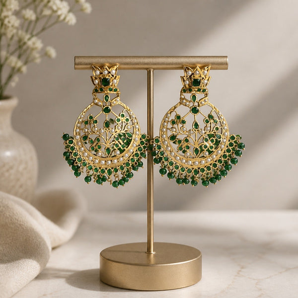 Emerald green gold-tone chandbali statement earrings displayed on jewelry stand