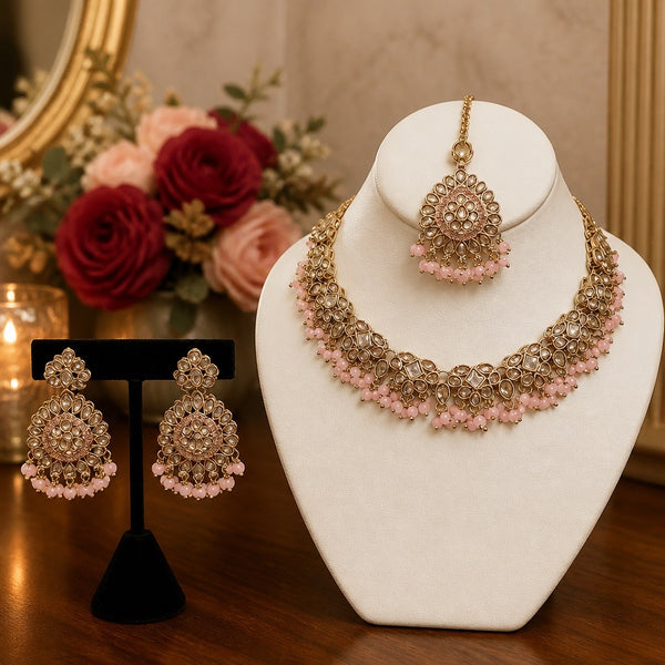Gold and pink kundan style bridal necklace set with earrings and tikka displayed on jewelry bust