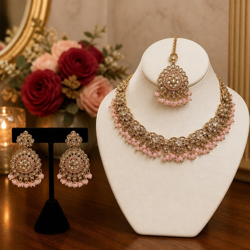 Gold and pink kundan style bridal necklace set with earrings and tikka displayed on jewelry bust