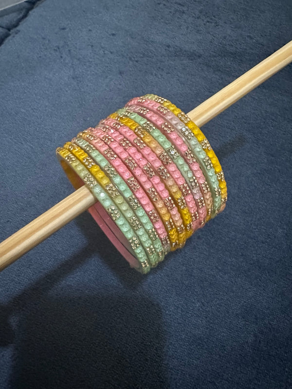 Pastel light multicolor glass bangles displayed on a wooden rod with crystal accents