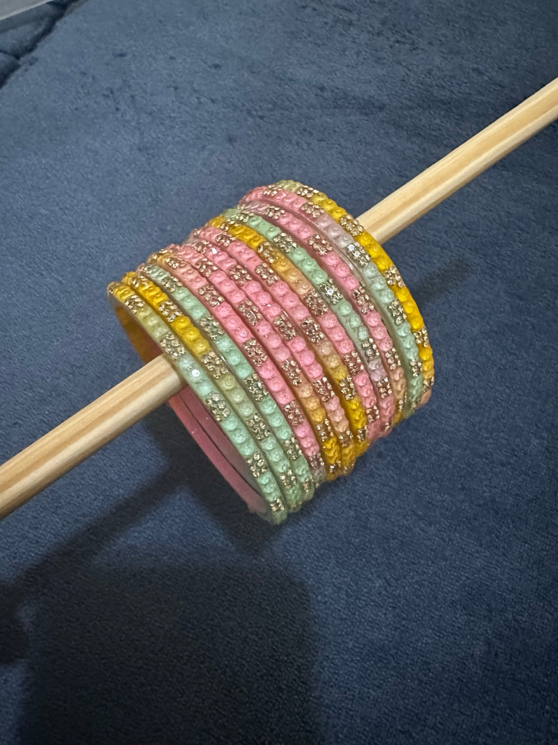 Pastel light multicolor glass bangles displayed on a wooden rod with crystal accents