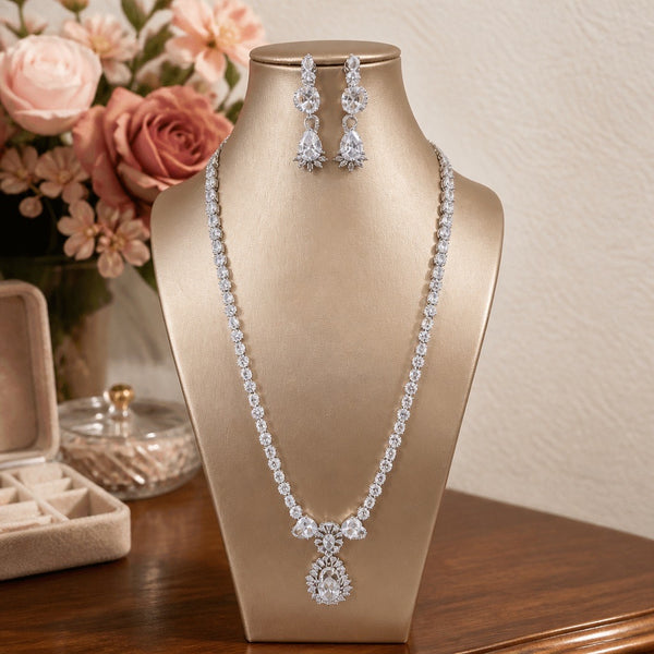 Long American diamond necklace and earrings set on gold display with floral background