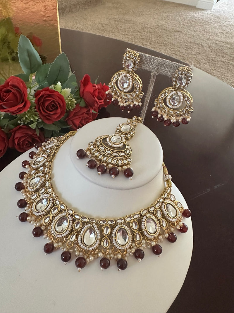 Angled view of antique gold maroon kundan necklace, earrings and tikka set
