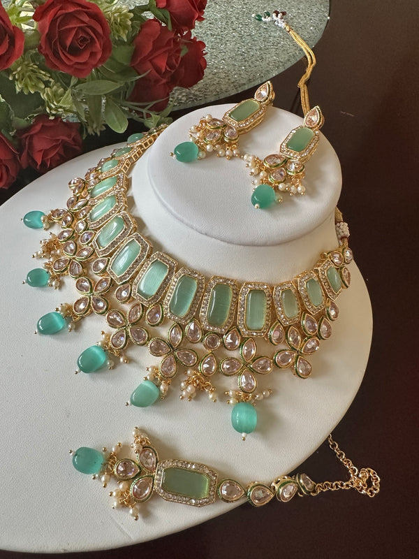 Mint green Kundan bridal necklace set with matching earrings and tikka displayed on a white jewelry bust