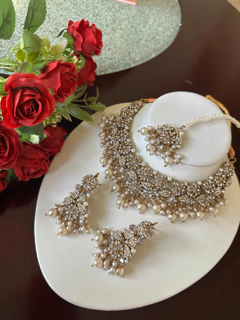 Angled view of pearl and American diamond floral choker necklace set with matching earrings and tikka