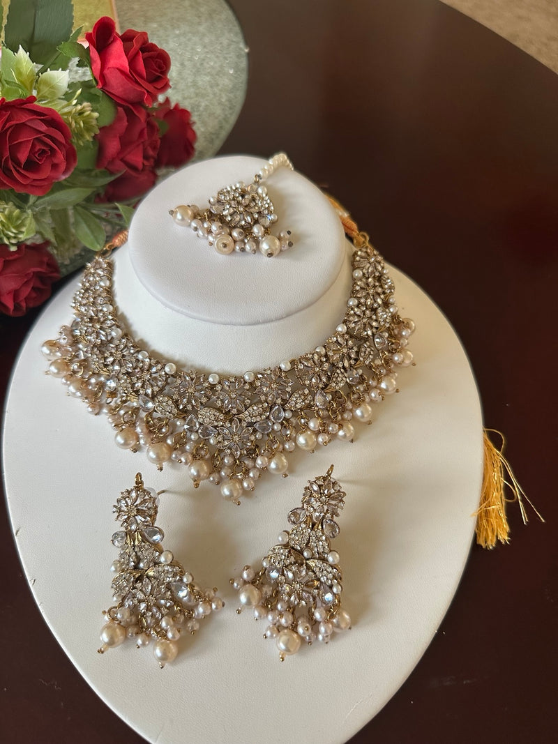 Full display of pearl and American diamond choker necklace set with matching earrings and tikka on a white bust