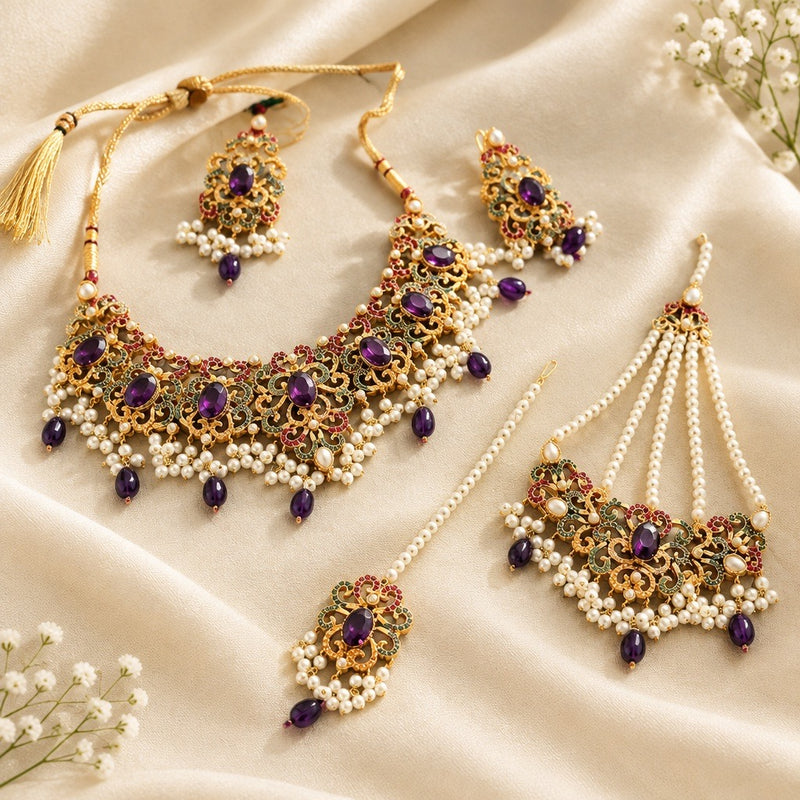 Purple stone and gold-tone bridal necklace set with pearl-style beads, earrings, maang tikka and jhoomar on ivory satin.