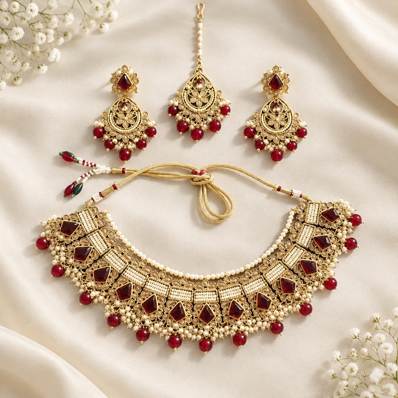 Gold-tone red stone necklace with pearl-style fringe, matching earrings and maang tikka arranged on ivory satin, showing the adjustable tie cord.