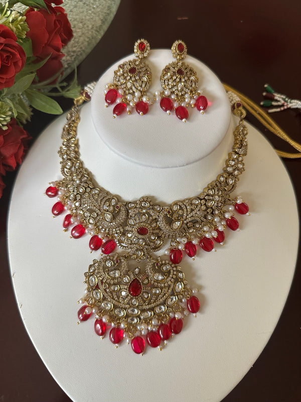 Ruby red Kundan bridal necklace with statement pendant and matching earrings displayed on a white bust