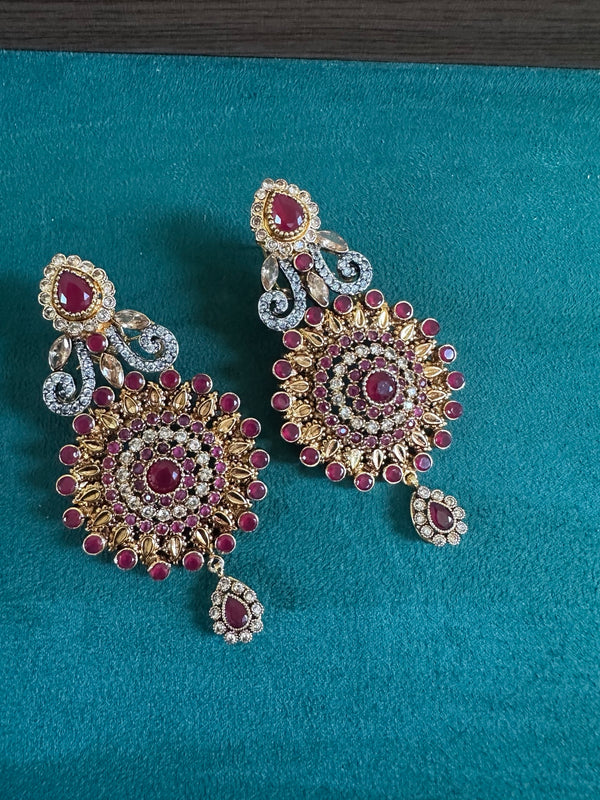 Ruby statement earrings on teal background with gold tone detailing